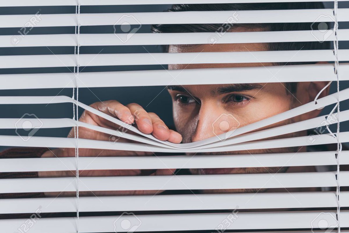Man looking through window blinds