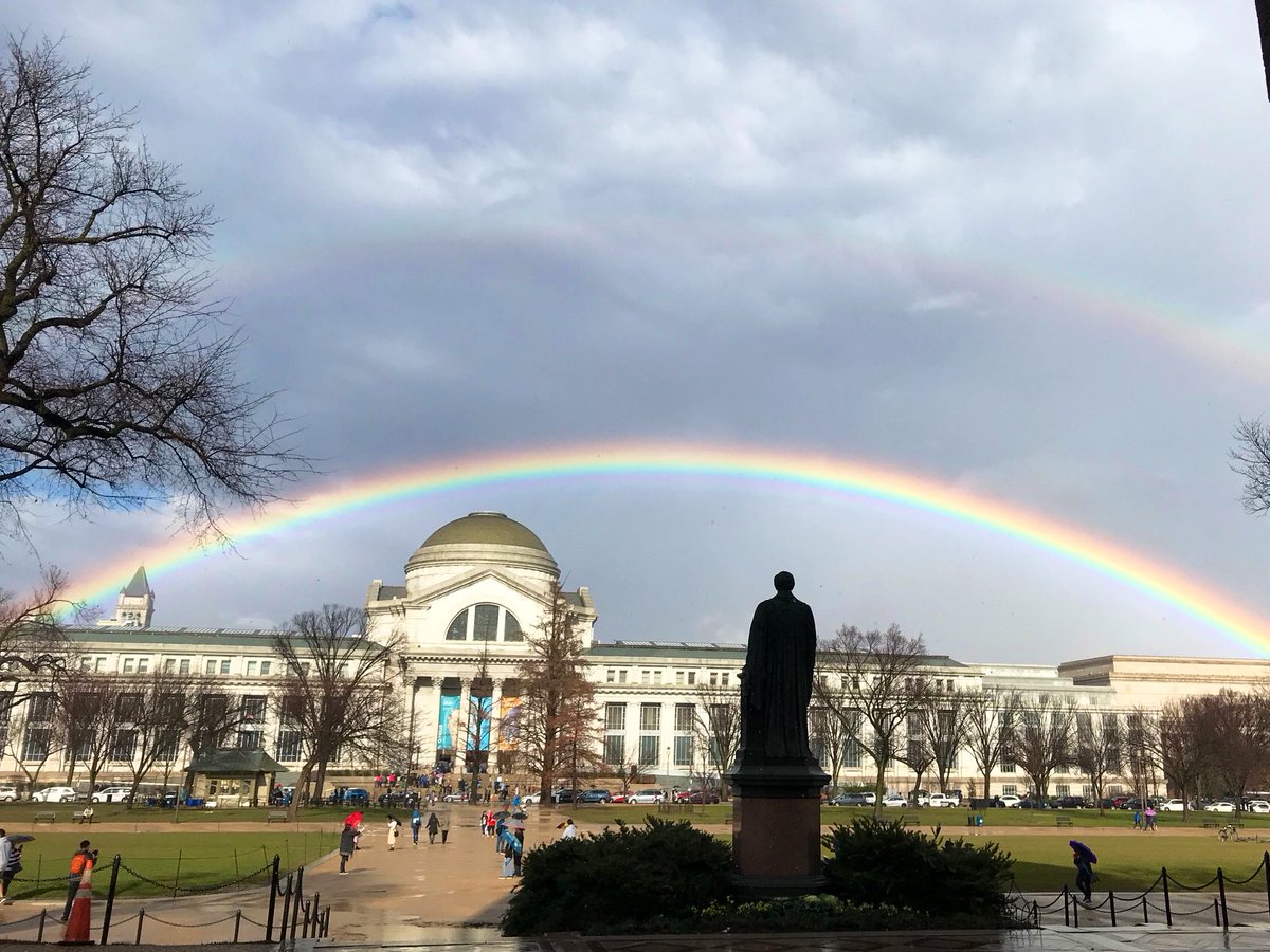 Museum building with statue in foreground and rainbow overhead.