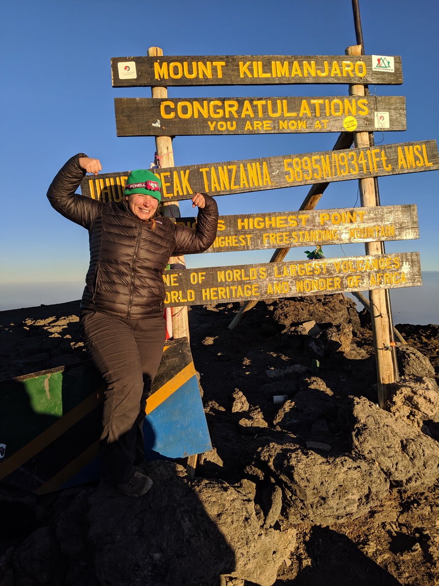 A flexing Maddie standing in front of the sign at the peak of Mt Kilimanjaro.