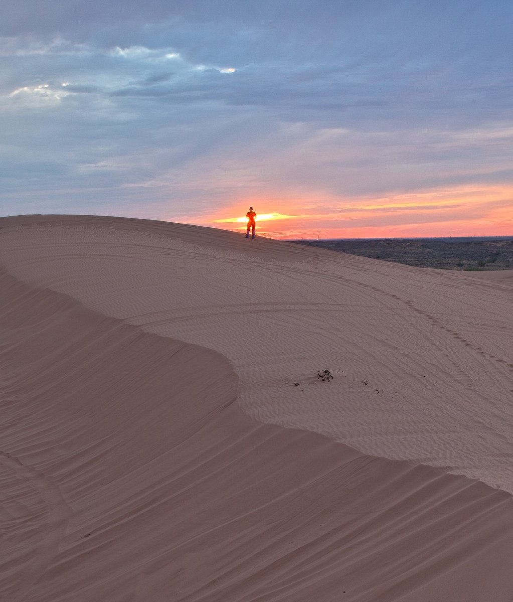 woman standing on dune facing the sunset. 