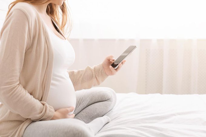 Pregnant woman sitting on bed using cell phone.