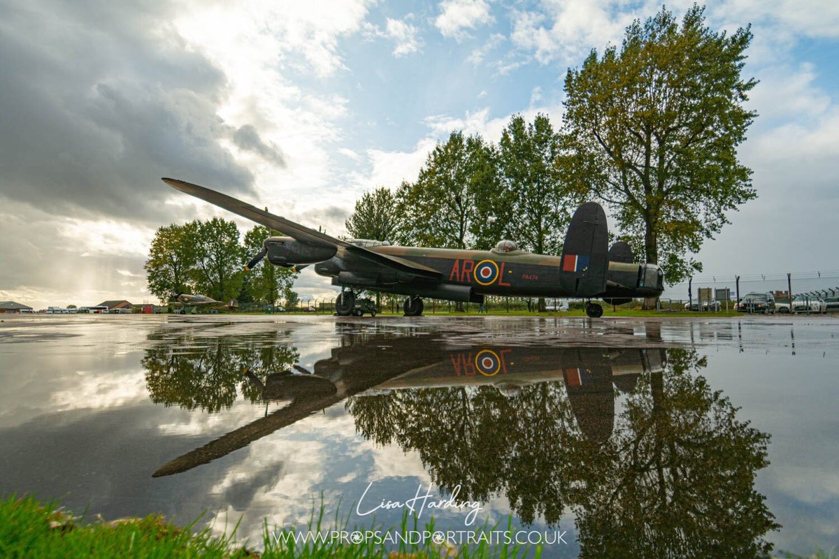 A lancaster bomber in on the airfield, reflection showing in a rain soaked puddle