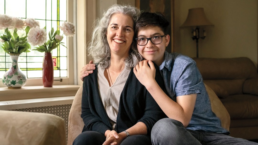Alum Lara Pullen sits with her son in a living room setting.