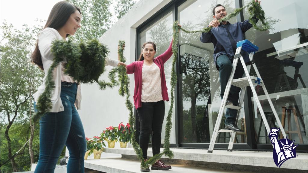 A man is standing outside on a small ladder removing Christmas garland with the help of two friends
