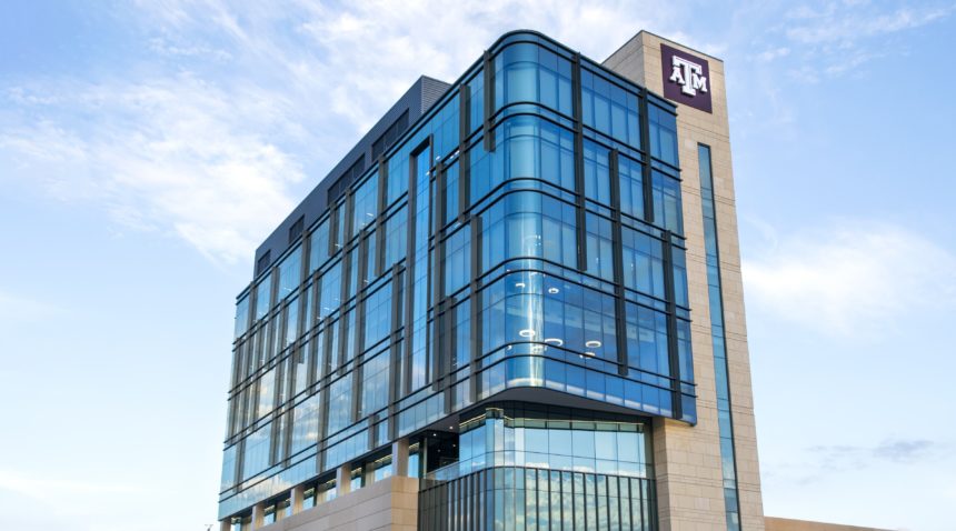 looking up at the large blue and tan building with tamu logo on a partly cloudy day