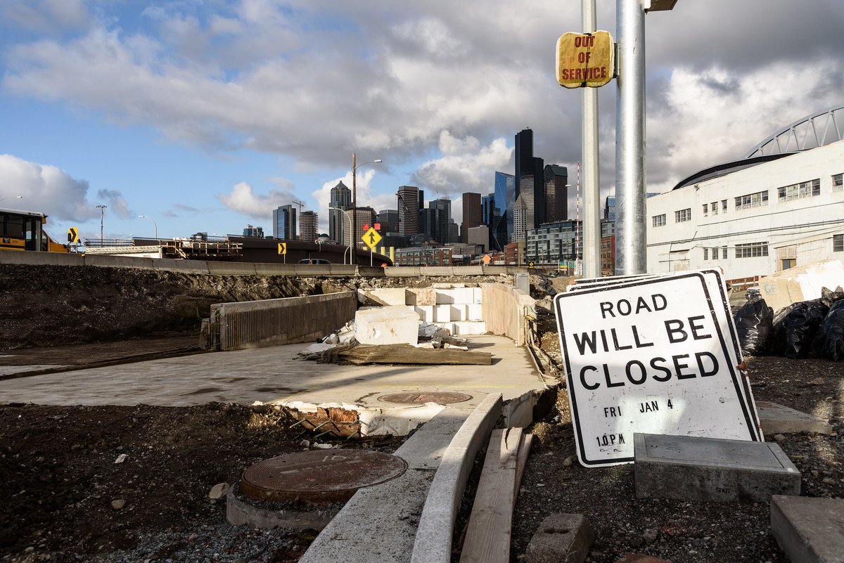 White foam blocks the entrance to a highway tunnel ramp, with Seattle skyline in the background