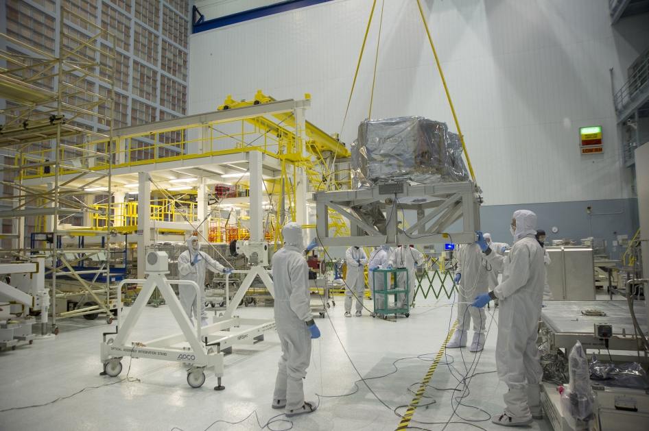 Engineers dressed in white protective suits work inside a large clean room. 