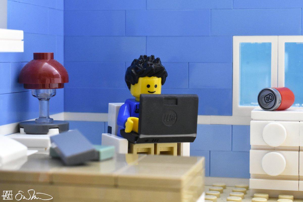 LGS sits in a chair beside his bed and is surrounded by books and an empty soda can. He is working on his laptop.