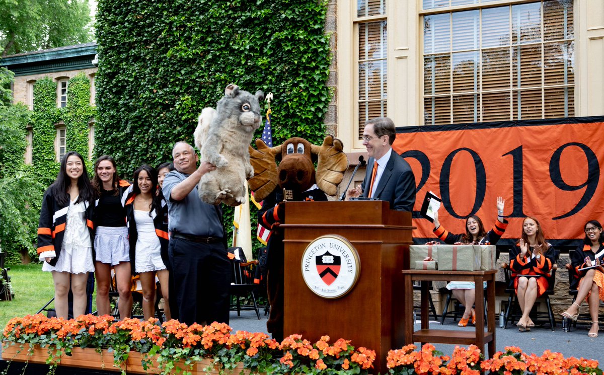 Officer William Boyle and the moose mascot of Mathey College hold up a large toy squirrel as President Eisgruber explains its purpose to the crowd