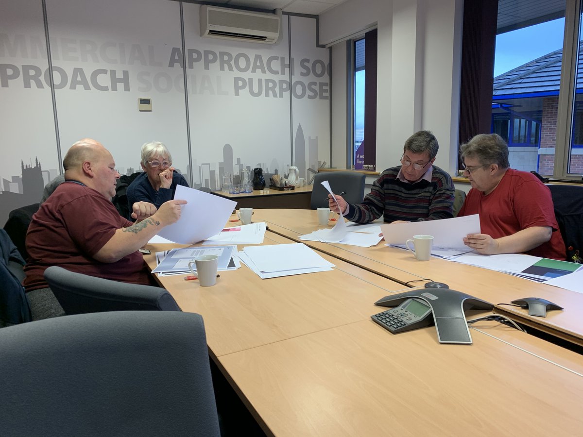Customers sit around a table in an office meeting room examining paperwork. 