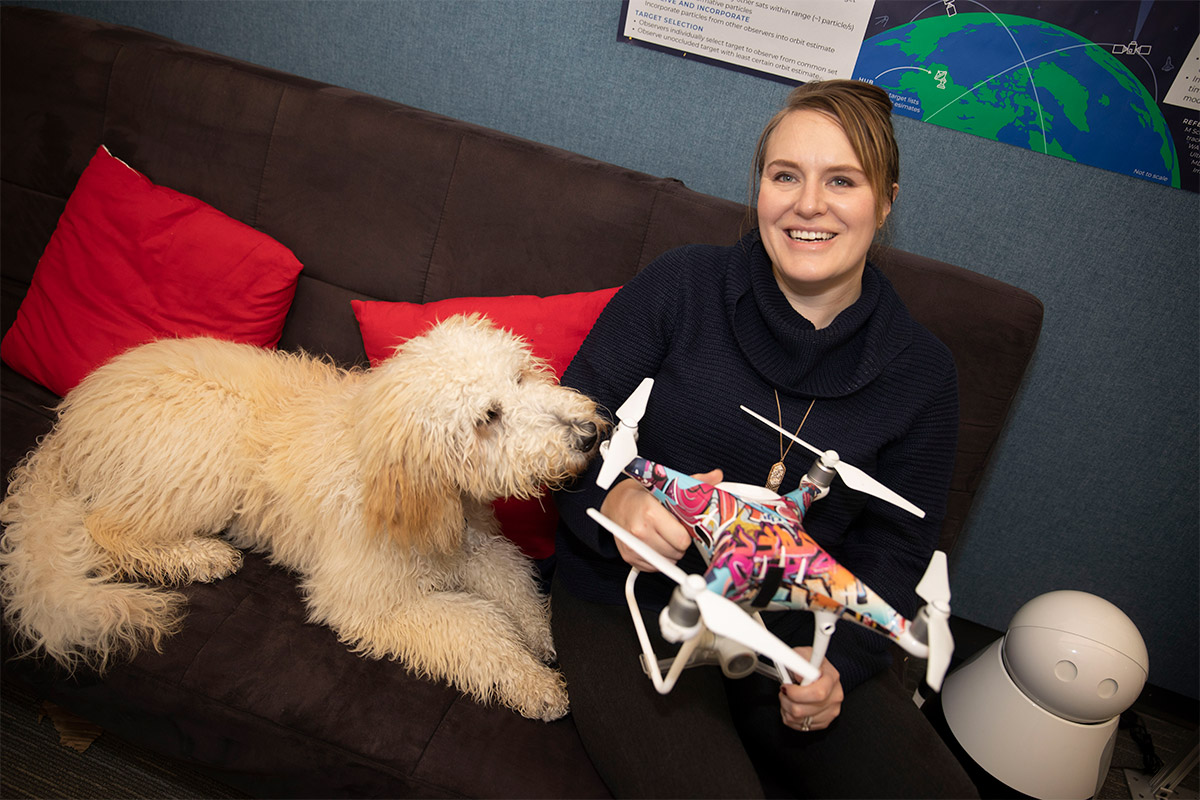 A woman holds a drone while a dog sits beside her