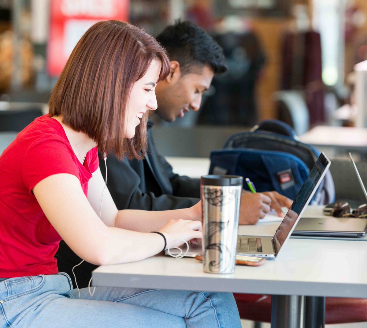 One female and one male student study next to each other with computers and coffee.