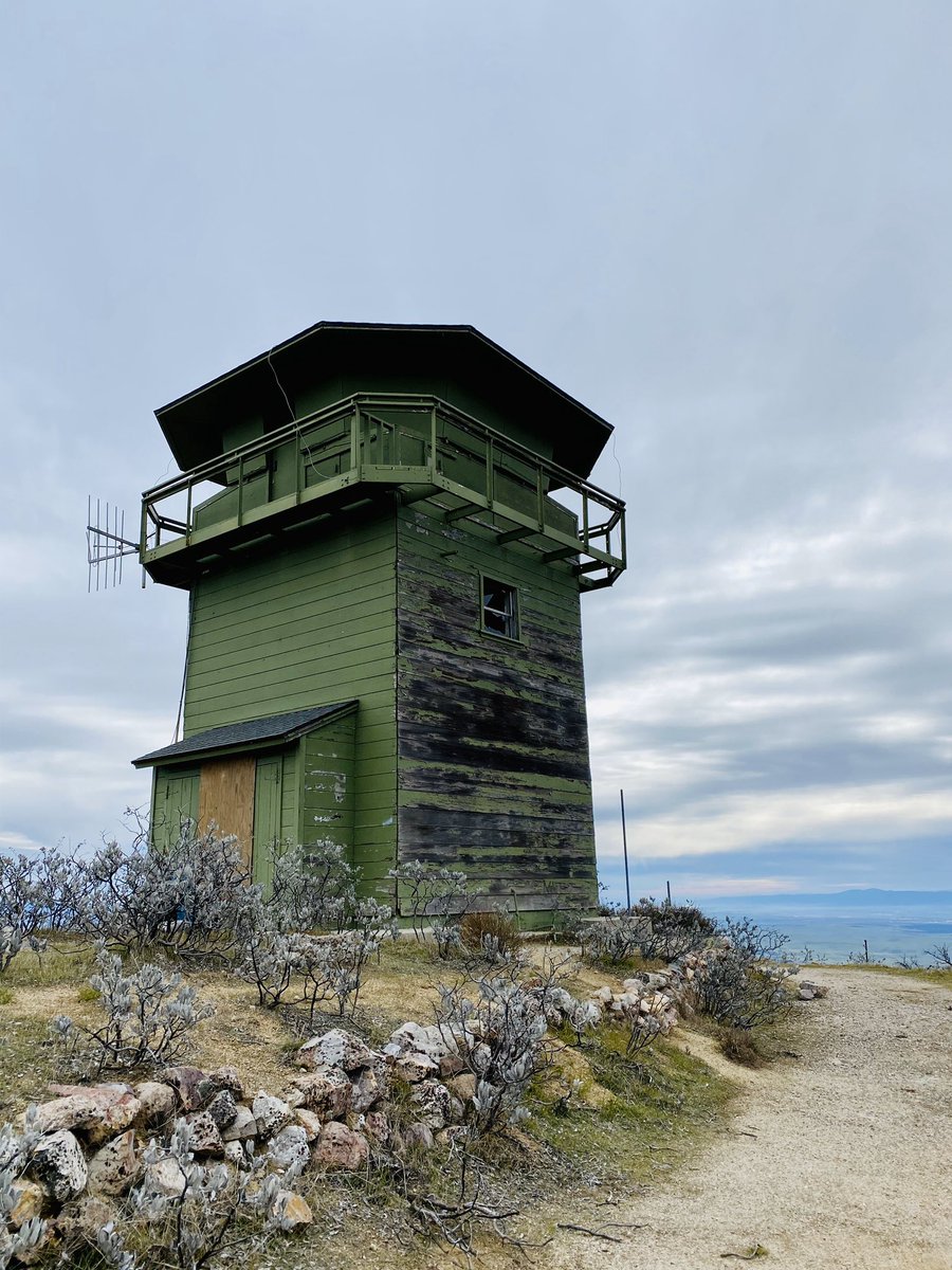 A green abandoned watch tower atop a mountain with blue sky and clouds behind.