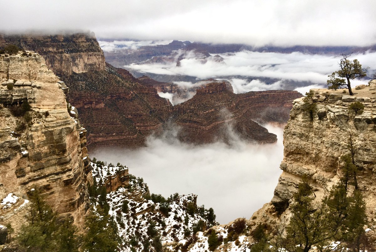 Description canyon peaks and cliffs rising above a thick layer of clouds and fog within a vast canyon landscape.