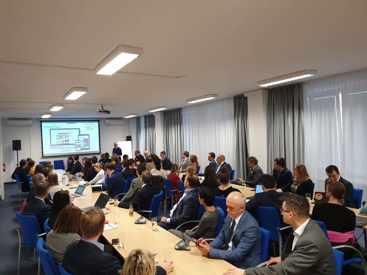 Minister Zagórski stoi na tle ekranu, na którym wyświetlana jest prezentacja. Przed nim siedzący członkowie grupy.