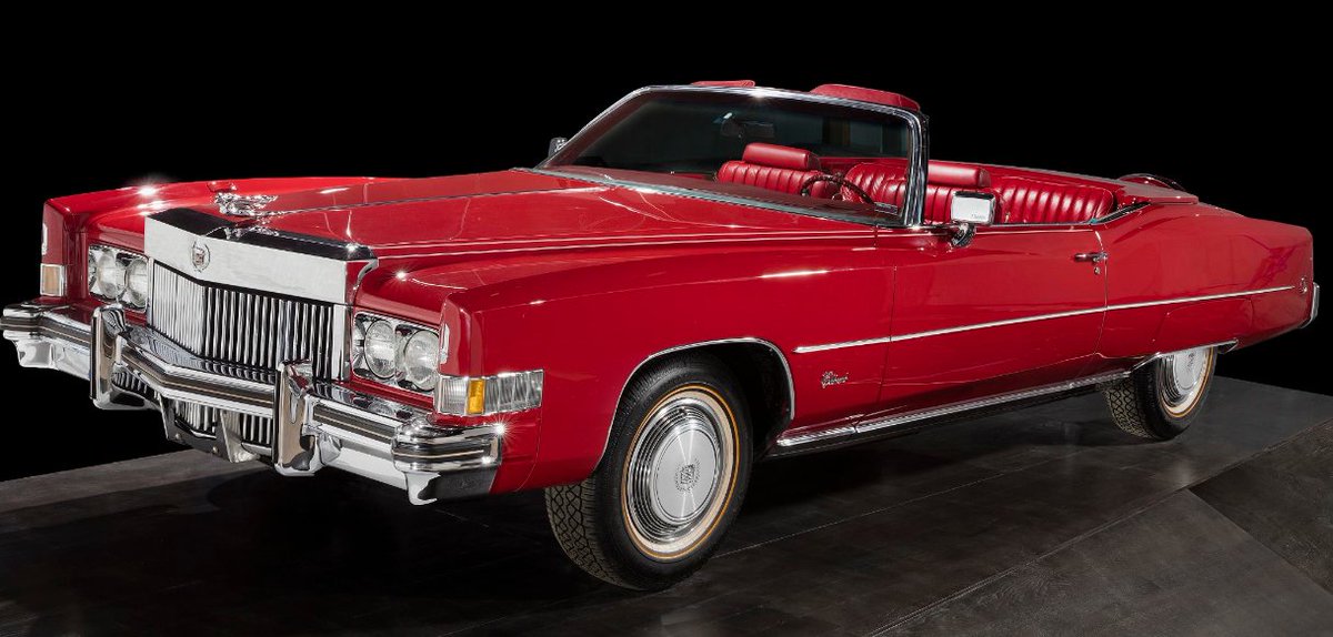 On a black background and black reflective surface, a red Cadillac Eldorado, model year 1973, owned and driven by Chuck Berry.