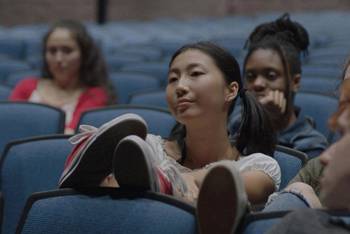 Actors in a scene sit in seats in a movie theater