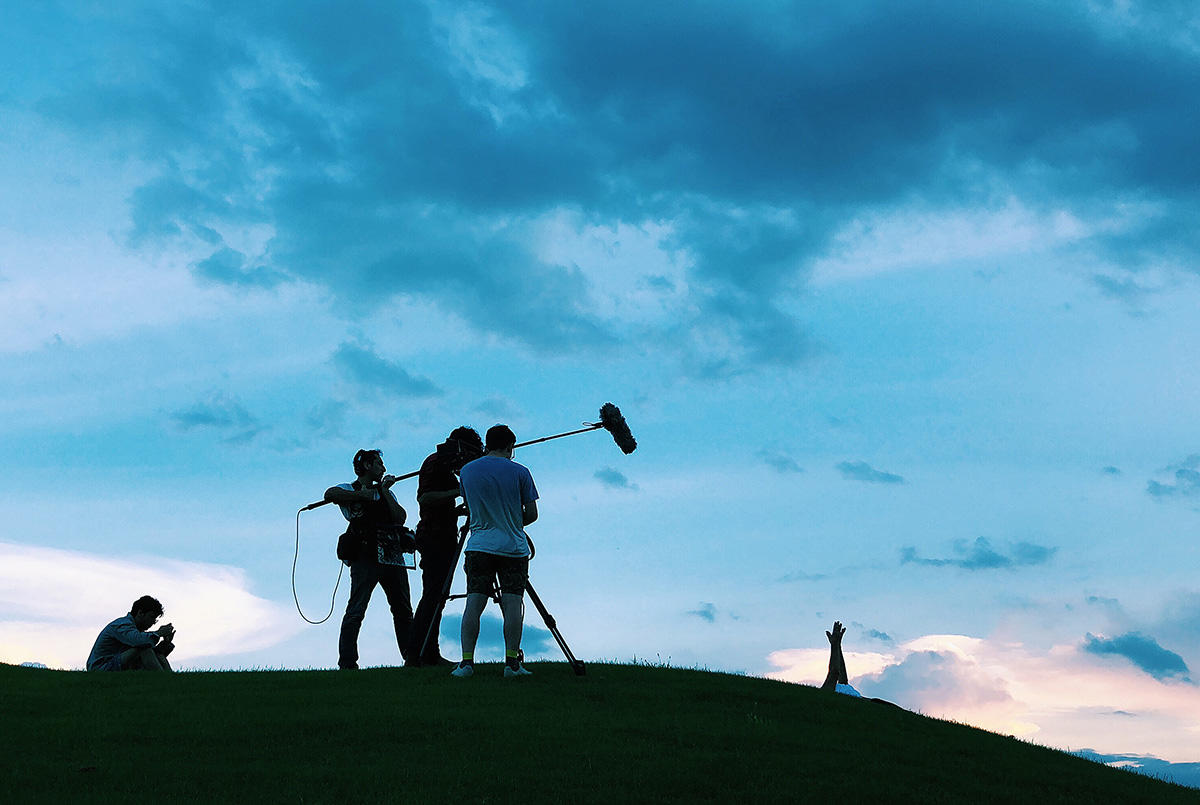 Filmmakers work outdoors in front of a blue evening sky 