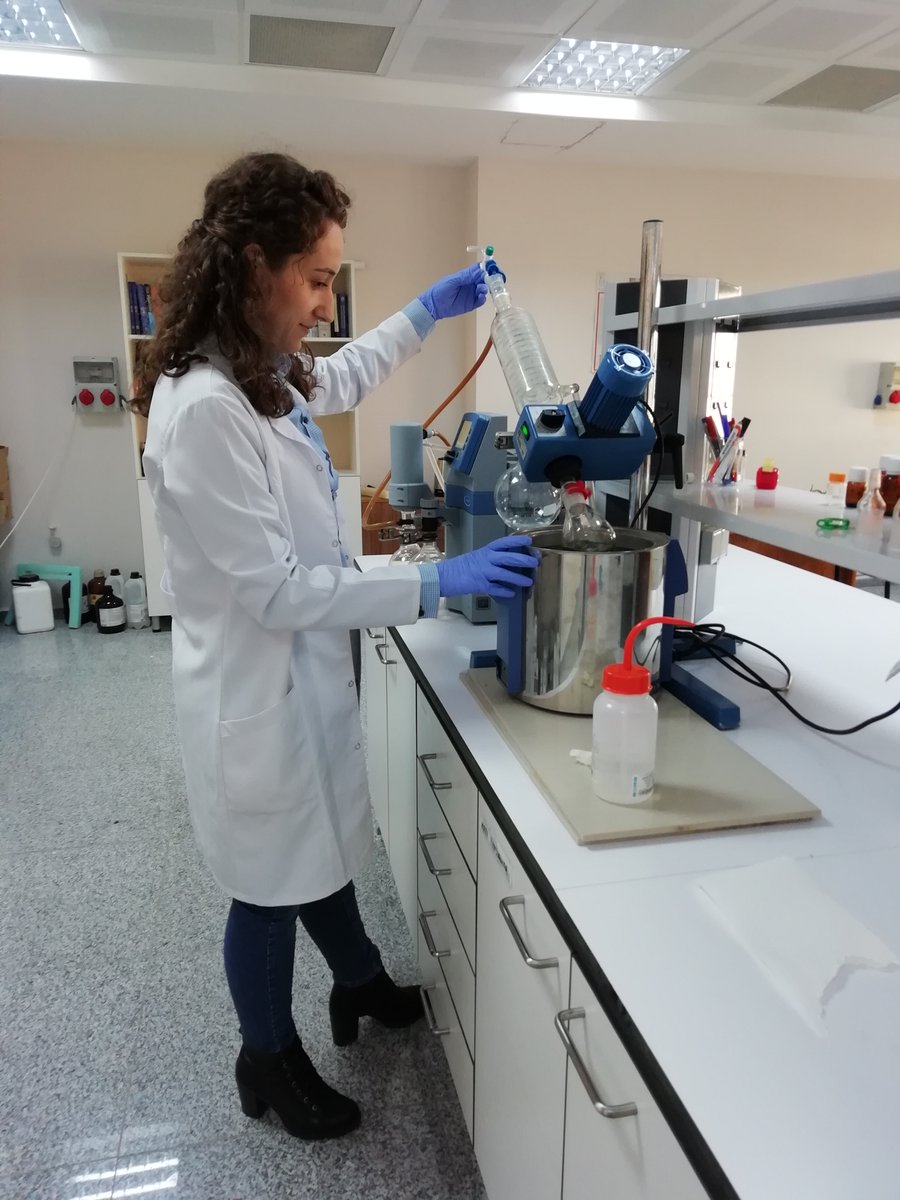 Seyma perfoming an experiment at a lab bench. She wearing a lab coat and gloves.