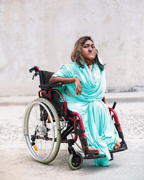 A dark-skinned, disabled Malaysian person in bright blue clothong using a black and red wheelchair