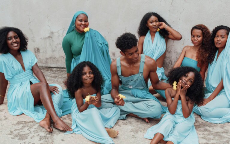 Dark-skinned Afro-Malaysian people seated on the ground in different bright blue attire and playing with/holding bright yellow flowers