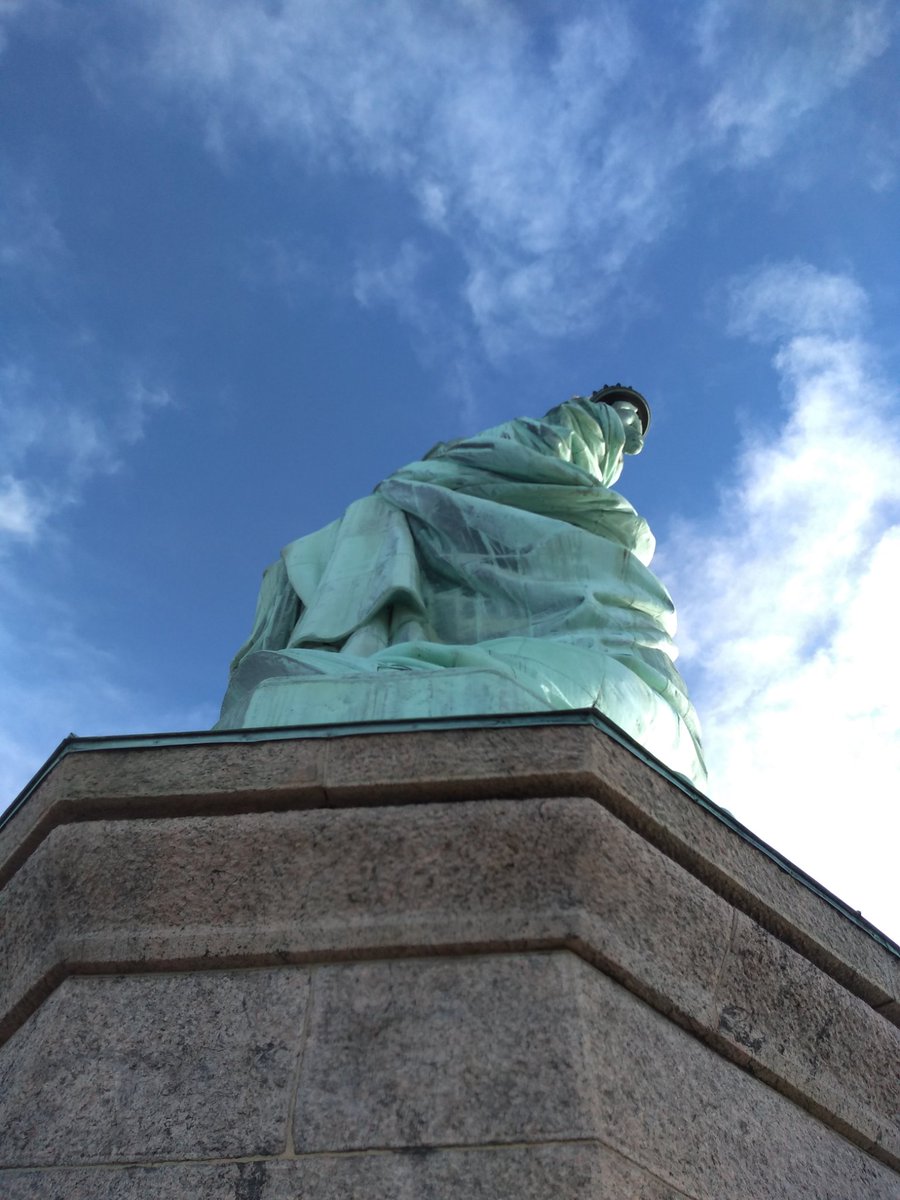 Photo of the Statue of Liberty taken from the top of the pedestal featuring the torch with blue sky and the background.