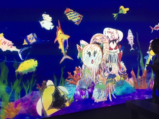 A screen showing children's drawings of sea creatures, which appears like an aquarium. 