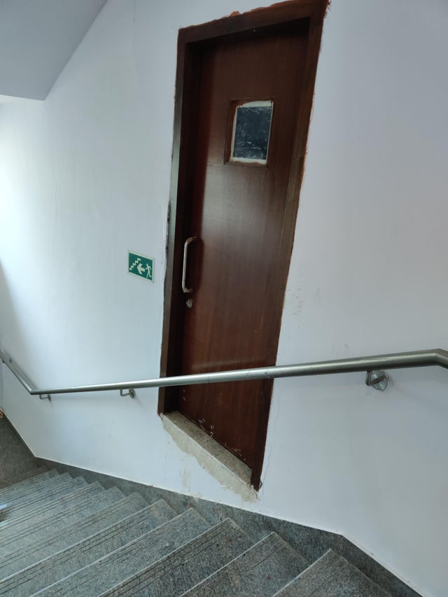 A door is seen on a wall on a staircase, behind a handrail, making it inaccessible.