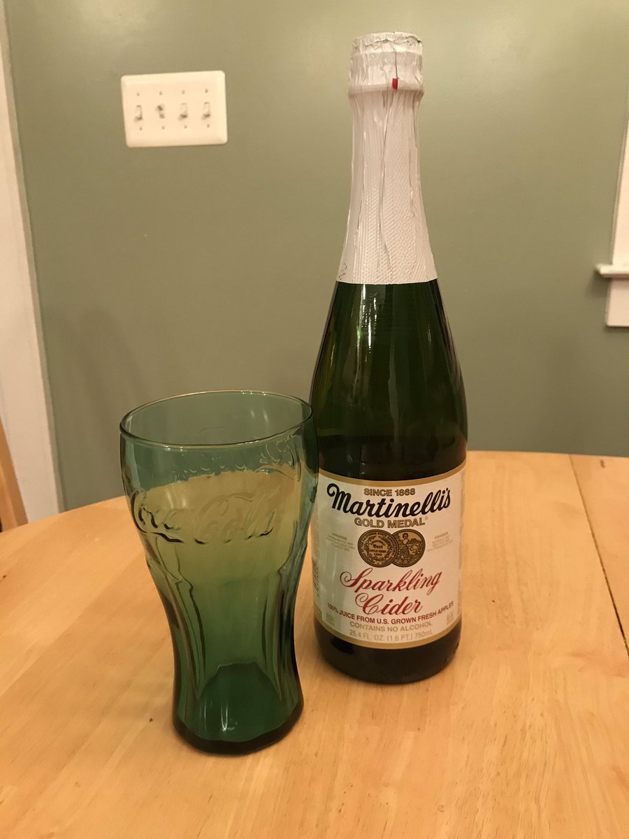 A bottle of sparkling cider next to a teal glass