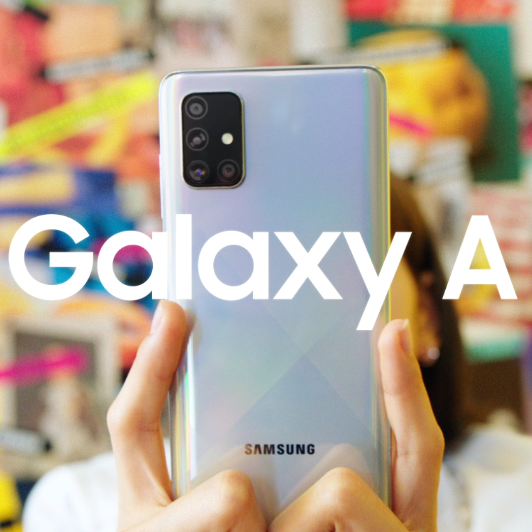 Hands hold up a silver Samsung smartphone with a quad-camera module, with large white 'Galaxy A' text overlaid across the image.