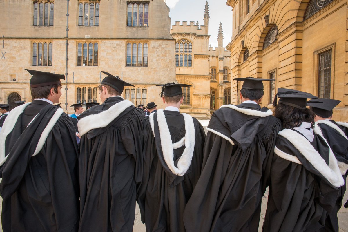 Students wait outside exam schools on degree day, wearing mortar boards and black gowns.