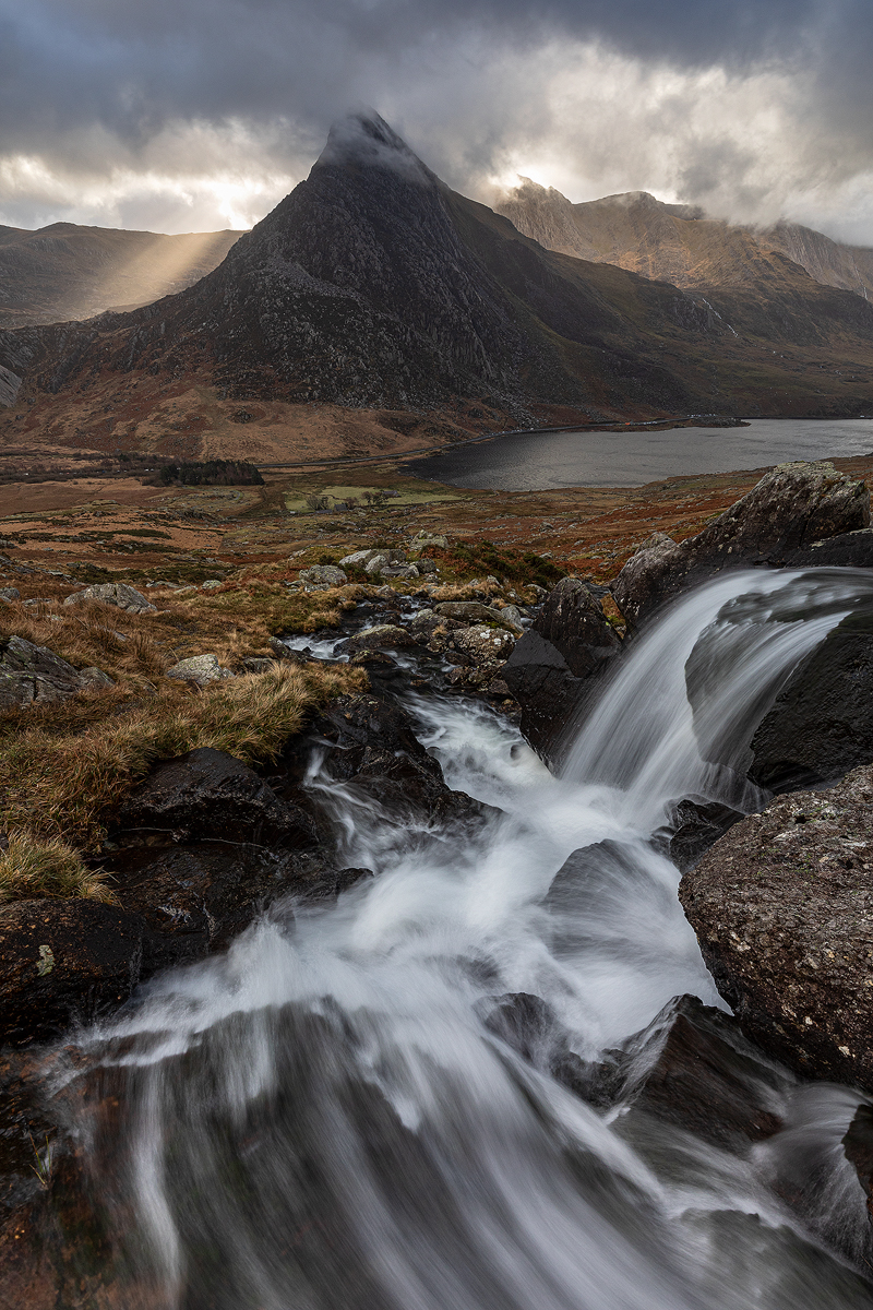 nickhansonphoto's tweet photo. Crepuscular rays and light come out from behind Tryfan, whilst the water from Afon Lloer rushes down through the foreground. @kasefiltersuk (portrait, needs a click) https://t.co/h2Mm8vHRon