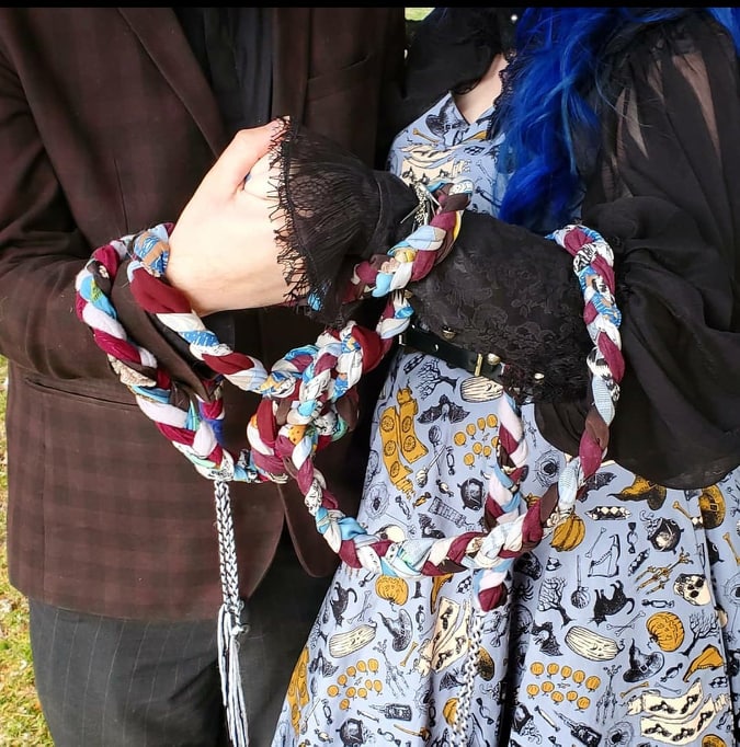 A multicoloured cord of fabric, wrapped and knotted around two wrists, braids of yarn coming off the ends, with charms knotted on.