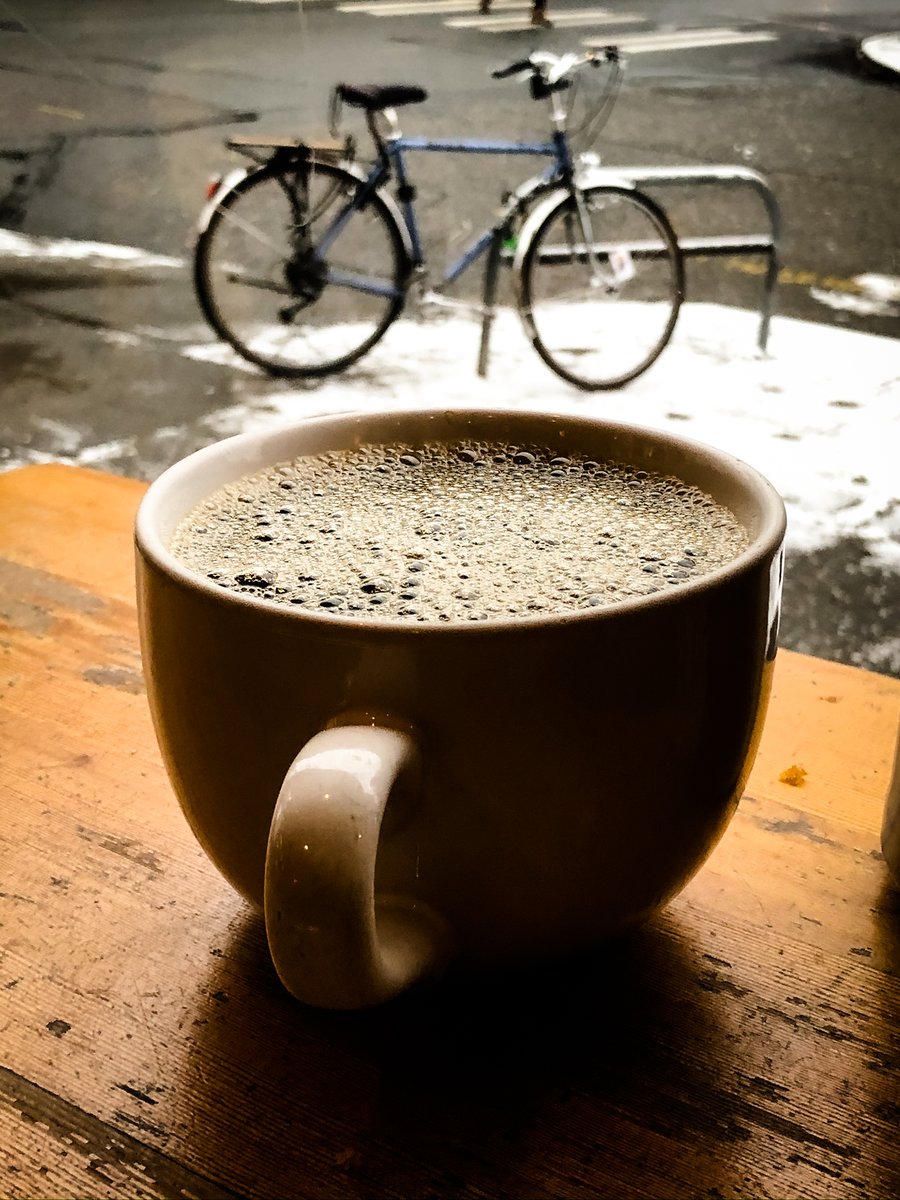 Photo of a cup of coffee with snow and a bicycle in the background.