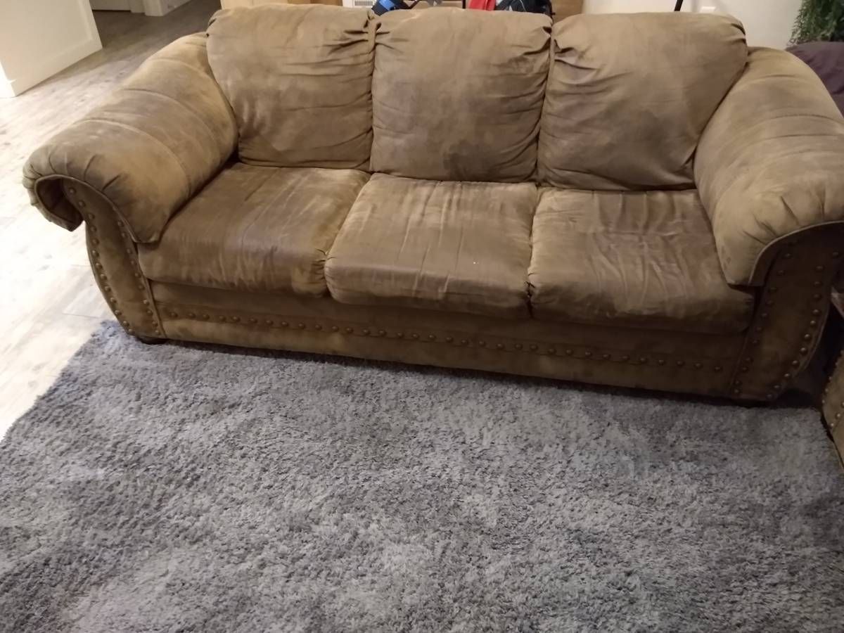 A photo of a grubby beige-upholstered sofa in a room with hardwood flooring. There is an area rug below the sofa.