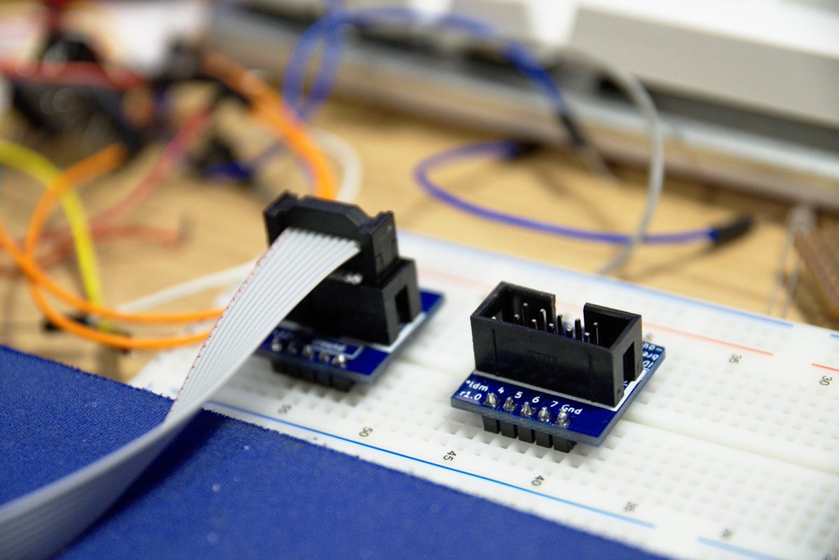 Two of the same blue PCB, with nothing surrounding them, one with a ribbon cable, the other without