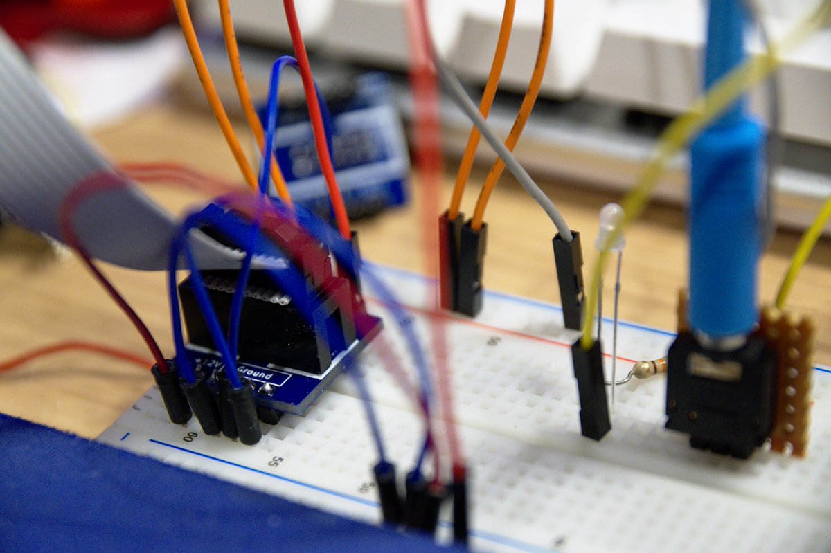 The same PCB, connected via colourful wires to the power rails of a breadboard