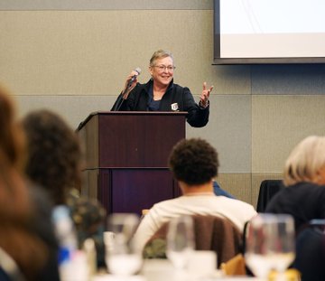 Dean Cheryl Ney speaks into a microphone at a lectern in front of a crowd