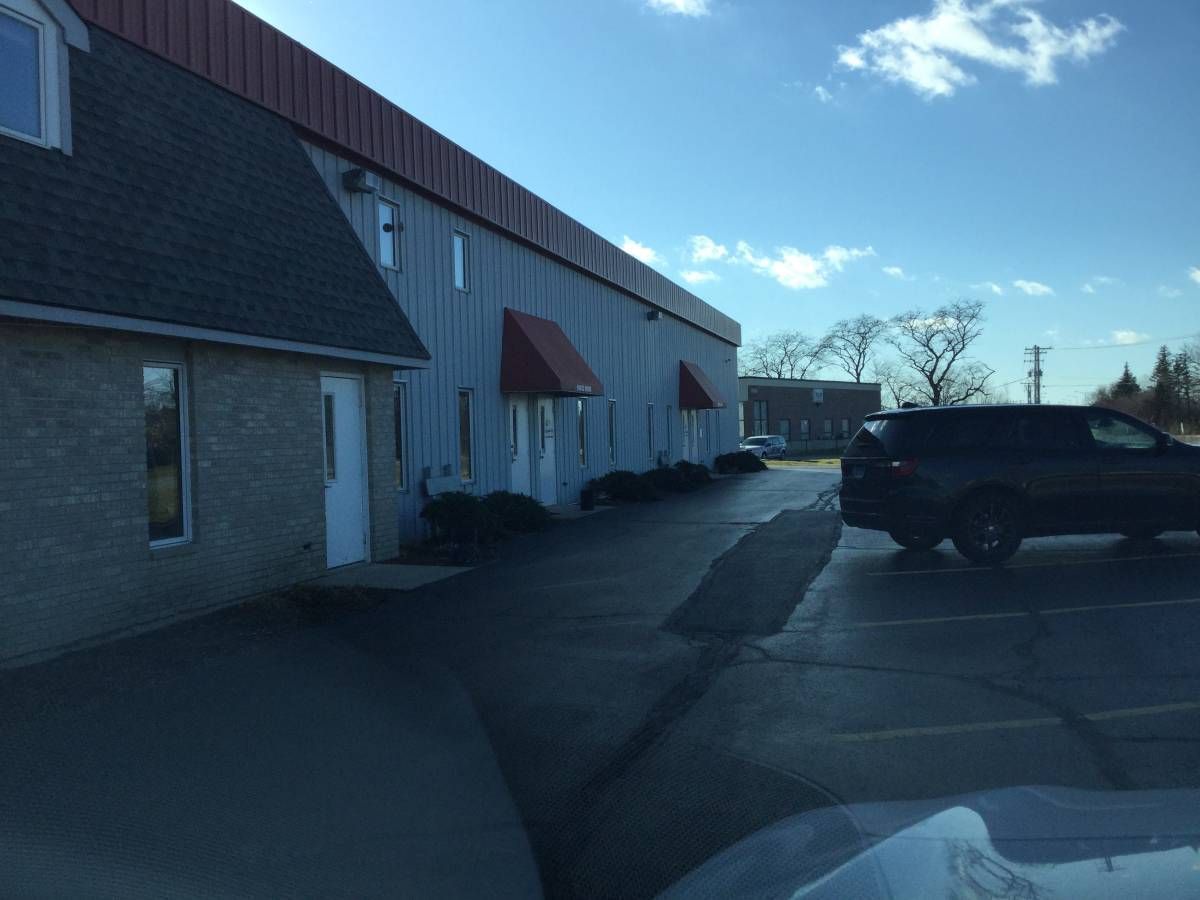 A photo of a parking lot outside a two-story office building. There is a minivan parked on the right. In the background, there are trees, a building, utility poles and power lines.