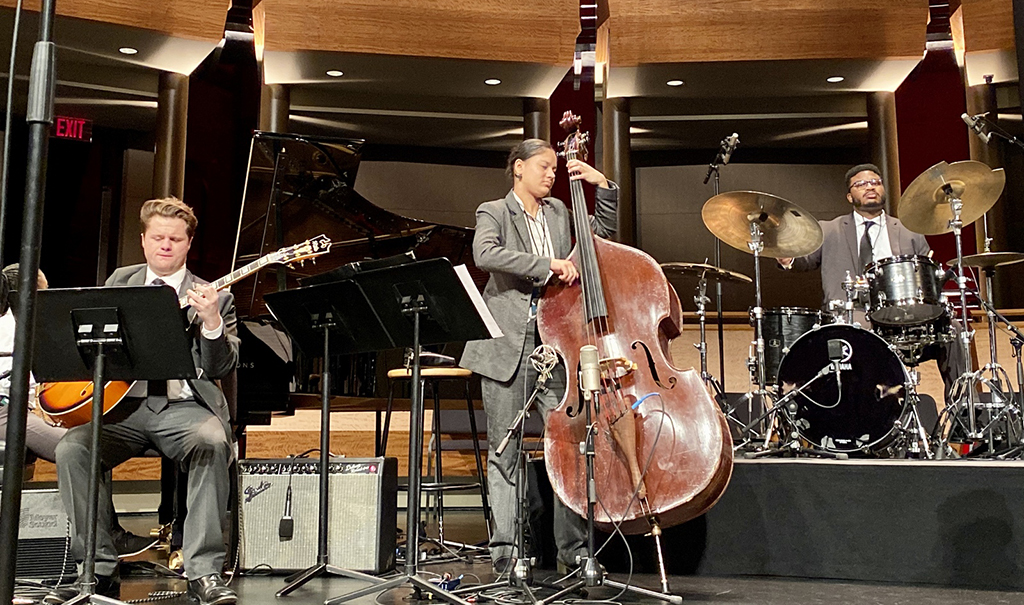 Three students in suits play instruments on a stage 