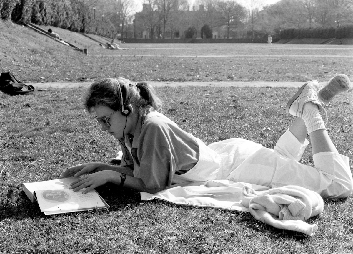 A girl in the 1980s lies on her stomach and reads in the Sunken Garden