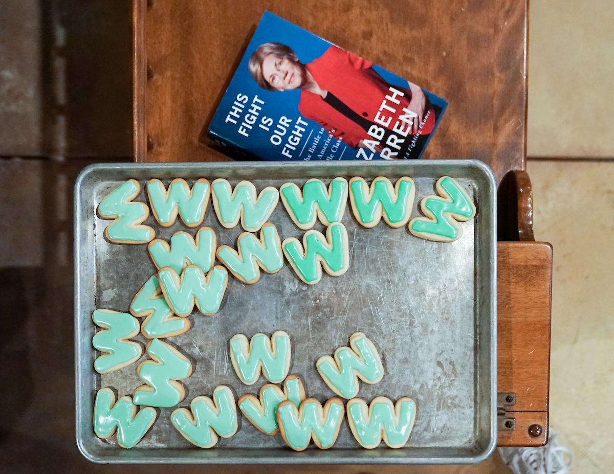 A tray of W-shaped cookies, frosted in Liberty Green frosting. Next to the tray sits a copy of Elizabeth Warren's book, "This Fight Is Our Fight."