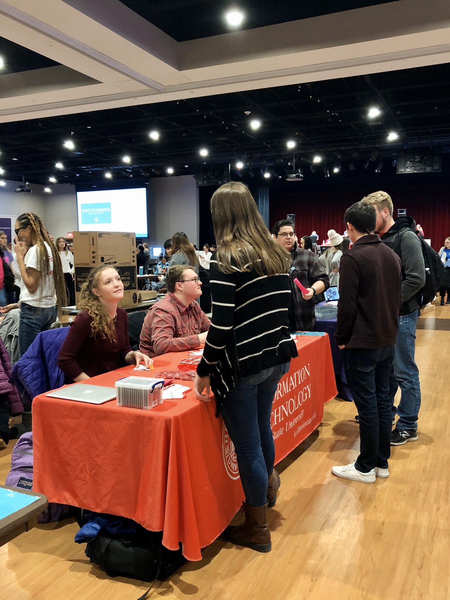 Students are interacting around a low red table. Ceiling and lights of the room are shown in the background.