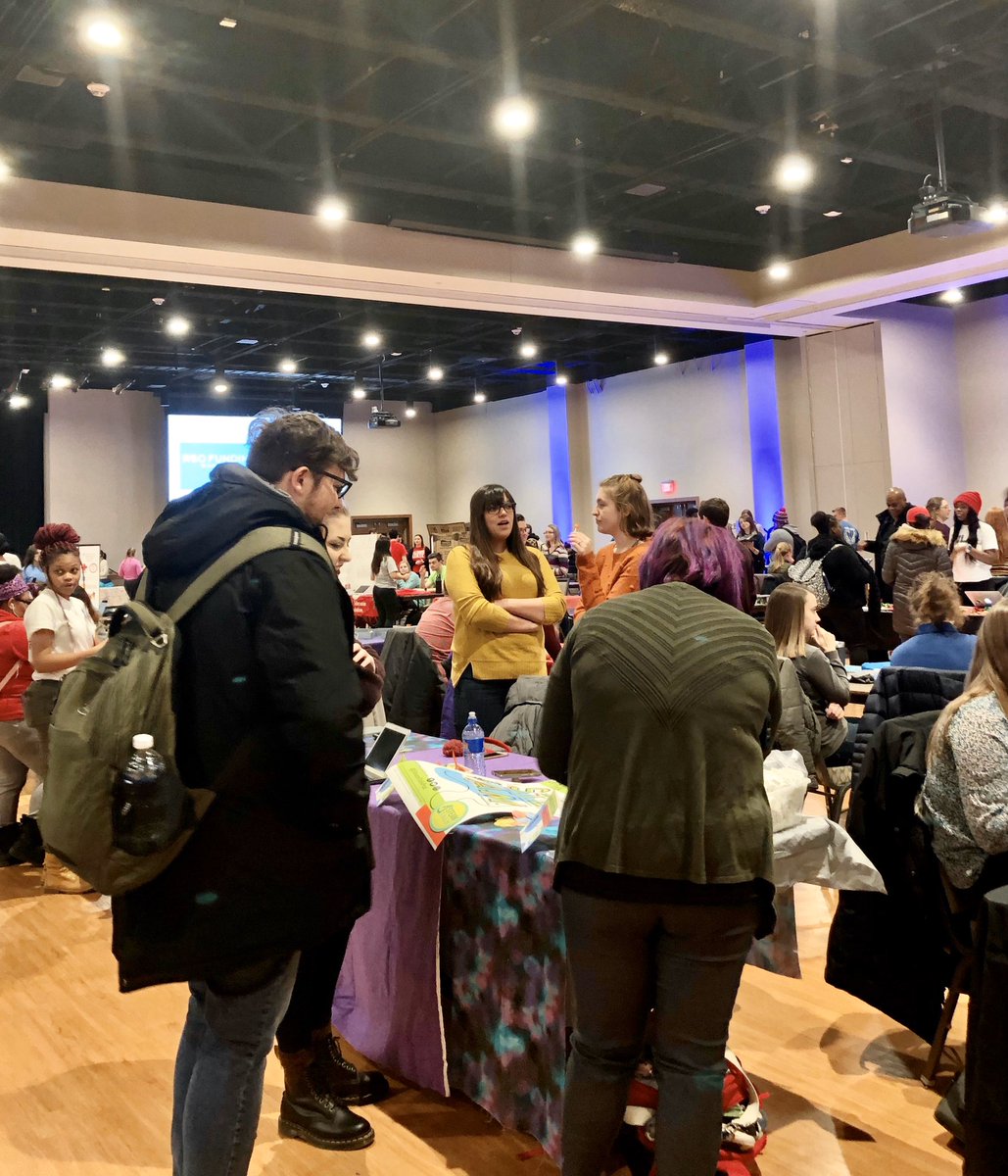 Students are approaching a purple table and students are socializing in the background.