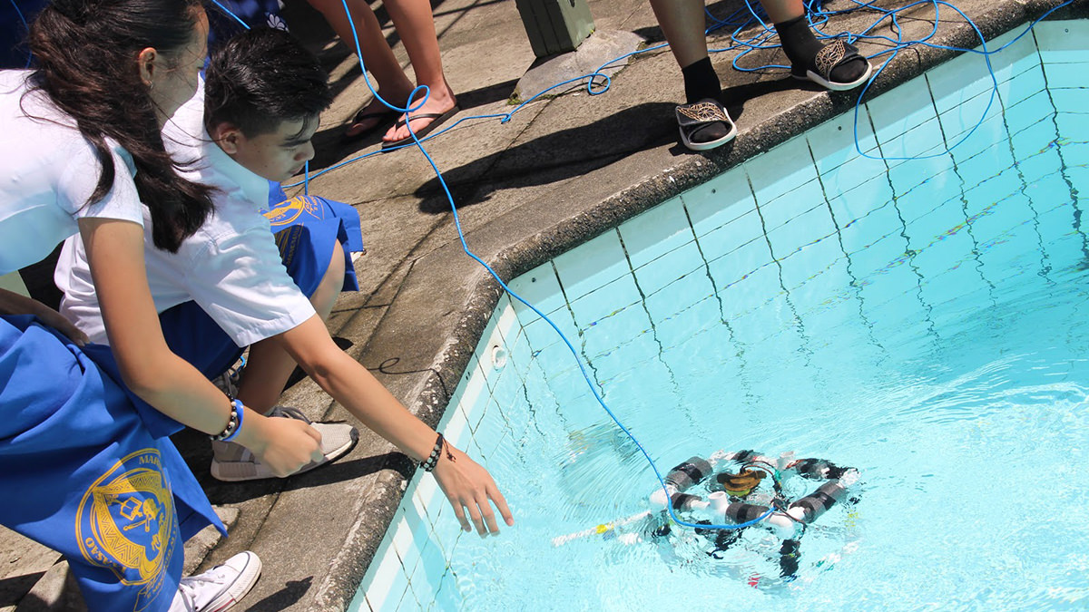 Two students testing a remotely operated vehicle in a pool