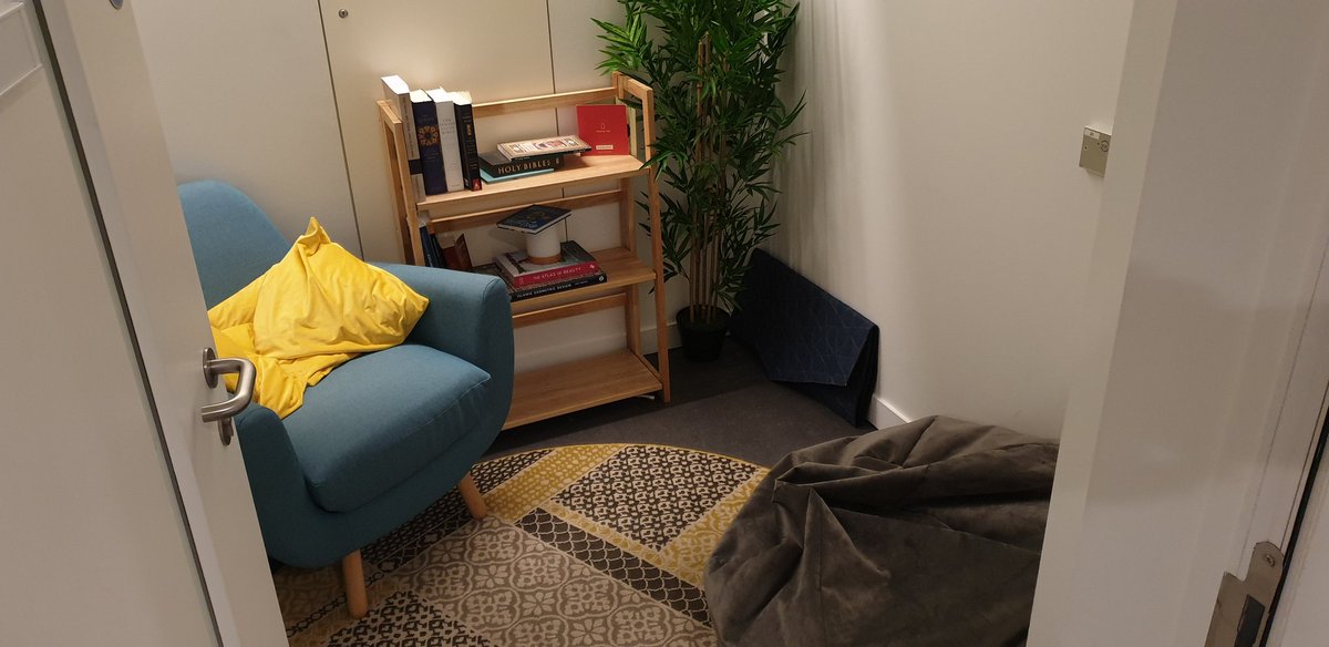 A small room with an armchair, throw cushions, a beanbag, rug, prayer mat, bookcase and pot plant.