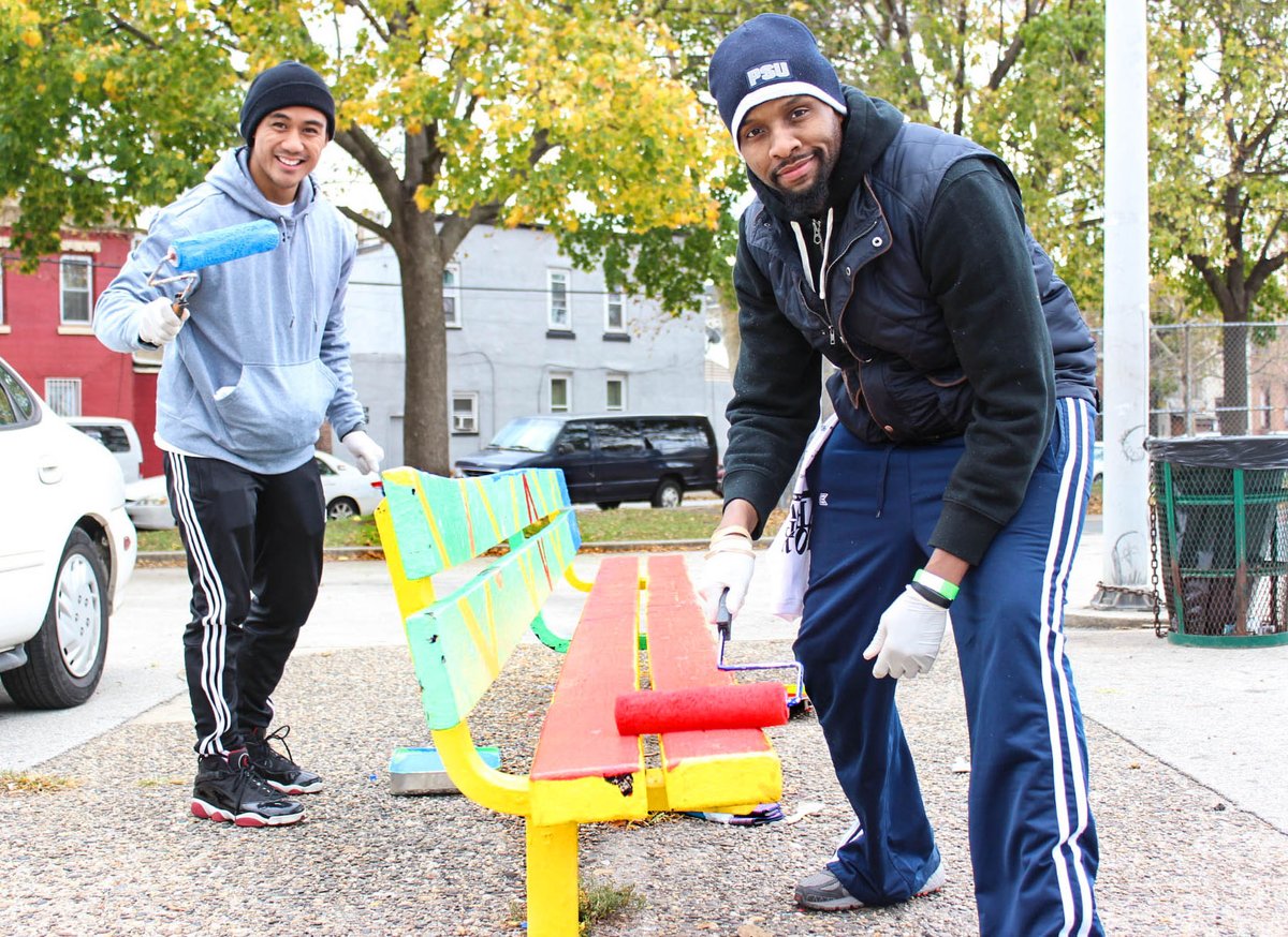 two volunteers smiling and painting a bench