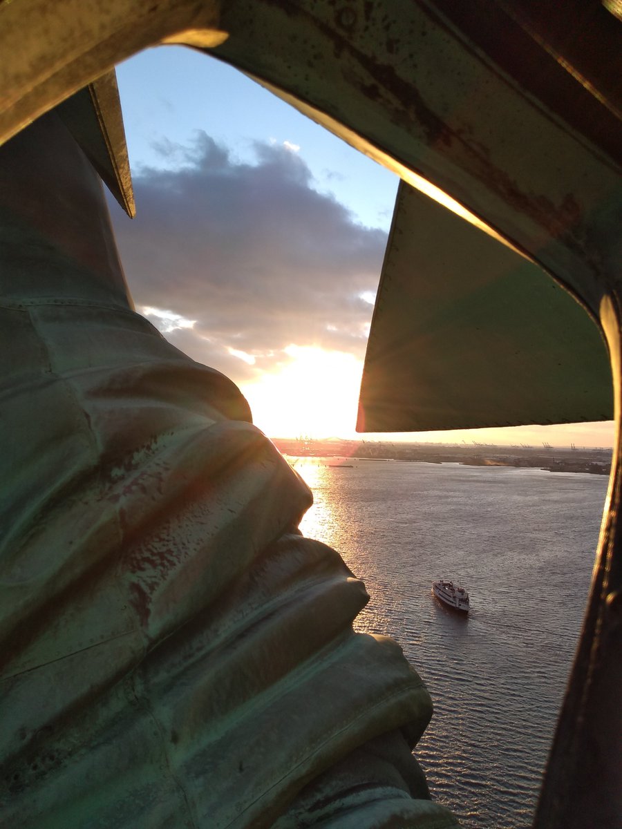 Photo of the ray and arm of the Statue of Liberty featuring a water view with a sunset in background.