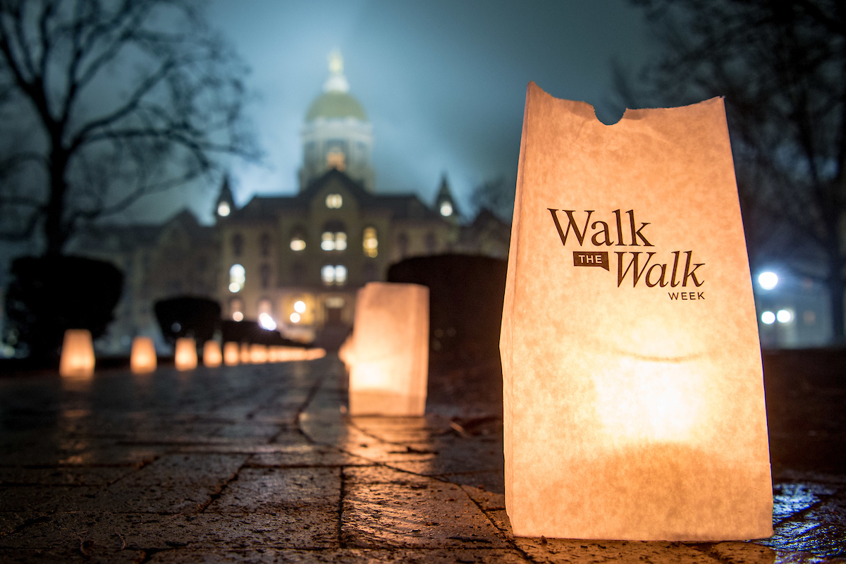 Luminaries with the words Walk the Walk Week on them line a path to the Golden Dome of the University of Notre Dame