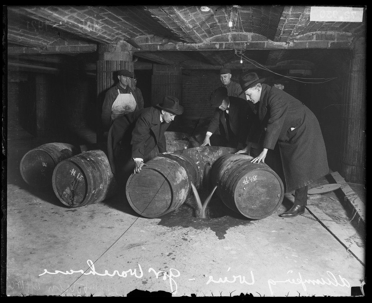 A group of men in a warehouse tilt barrels toward a drain to dump wine during Prohibition, Chicago, 1921. 